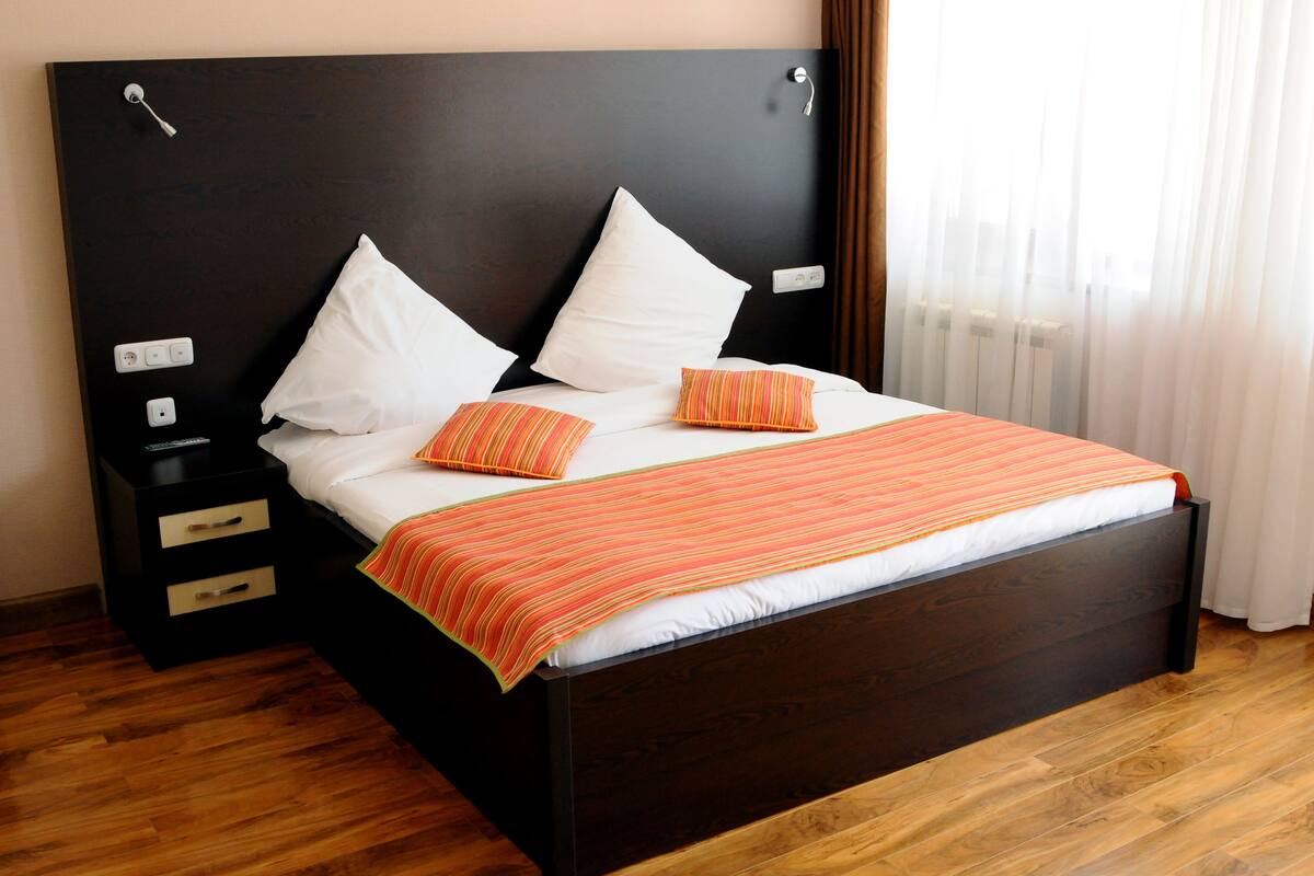 A neatly made bed with white and orange pillows, a striped blanket, and a dark headboard.