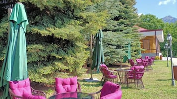 An outdoor seating area with wicker chairs and green umbrellas at Ani Resort Armenian Hotel.