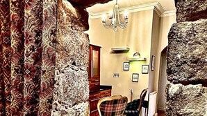 Une pièce avec un mur en pierre, un lustre, une cheminée et un coin repas comprenant une table et des chaises.