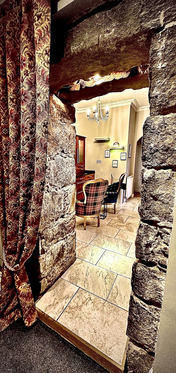Une pièce avec un mur en pierre, un lustre, une cheminée et un coin repas comprenant une table et des chaises.