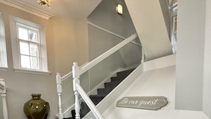 Un escalier avec une rampe blanche, une pancarte sur laquelle on peut lire « Soyez les bienvenus », et un vase posé sur le palier.
