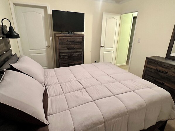 A bedroom with a bed, a dresser, a television on top of the dresser, and a door leading to another room. - MC (Modern Country) LIVING (Elizabethtown)
