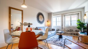 Een moderne woonkamer met een glazen eettafel, een rode stoel, een grijze bank en een grote spiegel.