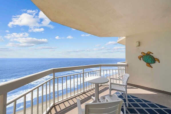 Un balcon avec une balustrade blanche, une petite table et une chaise. Un mur est décoré d’une fresque représentant une tortue.