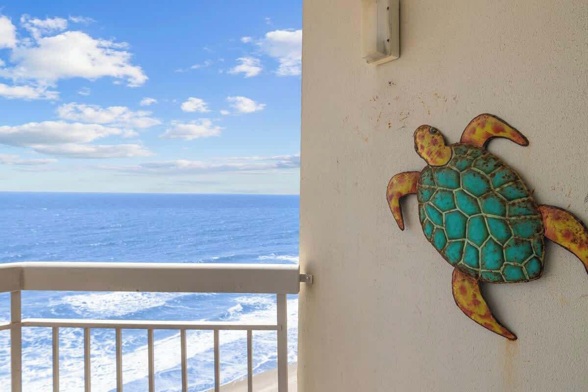 Een balkon met uitzicht op de oceaan, een witte balustrade en een aan de muur bevestigde schildpad decoratie.