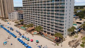 Un hôtel à plusieurs étages doté de balcons, d’un espace piscine et d’une plage avec des chaises longues.