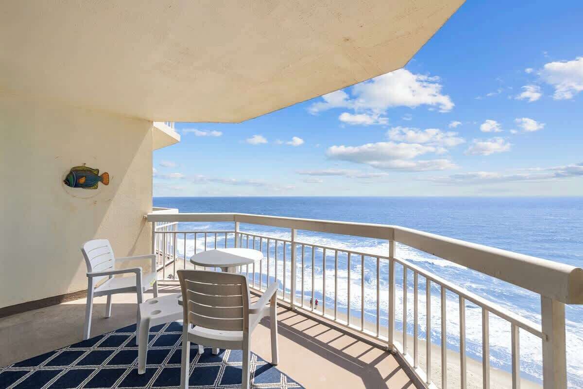Un balcon avec vue sur l’océan, des chaises blanches et une petite table.