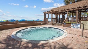 Un jacuzzi avec vue sur la piscine, une pergola en bois et un panneau indiquant le poste de surveillance des sauveteurs.
