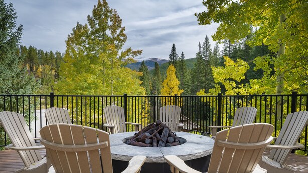 A deck with Adirondack chairs around a stone fire pit, overlooking a forested area with mountains in the distance. - Mountain Escape and Adventure at Winter Park (Winter Park)