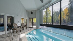 An indoor swimming pool with clear glass walls, wooden deck chairs, and a view of autumn trees. - Mountain Escape and Adventure at Winter Park (Winter Park)