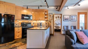 A modern kitchen with wooden cabinets, a black refrigerator, a microwave, and a stove. There is a dining area with a gray couch and a small table. - Mountain Escape and Adventure at Winter Park (Winter Park)