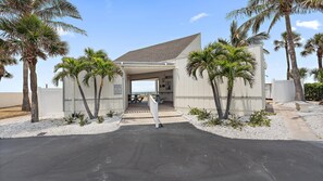 A covered entrance to a private property with a paved driveway, palm trees, and a beach view.