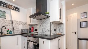 Eine moderne Küche mit weißen Schränken, einer Marmor-Spritzschutzwand, einem Schild mit der Kaffeekarte, einem Toaster und einem roten Feuerlöscher.