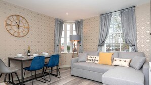 Ein modernes Wohnzimmer mit einem grauen Sofa, blauen Sesseln, einem Esstisch und einer Uhr sowie Wandpapier mit Muster.