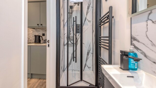 A modern bathroom with a glass shower enclosure, a marble backsplash, and a countertop with a soap dispenser. - The Cotswold Woodland by Fortuna Property Portfolio (Cheltenham)