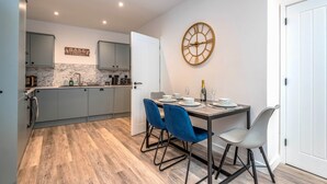 A modern kitchen with grey cabinets, a marble backsplash, and a dining area with a wooden table and blue chairs. - The Cotswold Woodland by Fortuna Property Portfolio (Cheltenham)