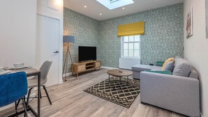 A modern living room with a sofa, a TV, a dining table, and a skylight. - The Cotswold Woodland by Fortuna Property Portfolio (Cheltenham)