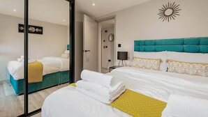 Ein Hotelzimmer mit einem großen Spiegel, einem petrolfarbenen, gepolsterten Kopfteil und einem gelben Zierkissen.
