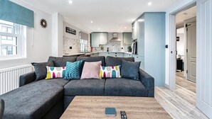 Ein modernes Wohnzimmer mit einem grauen Ecksofa, einem Holztisch und Blick in den Küchenbereich.