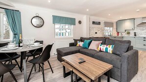 Ein modernes Wohnzimmer mit grauem Sofa, einem Holztisch und einem Essbereich mit rundem Tisch und Stühlen.