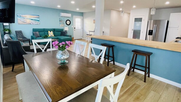 A modern kitchen with a wooden island, white bar stools, and a dining table with chairs.