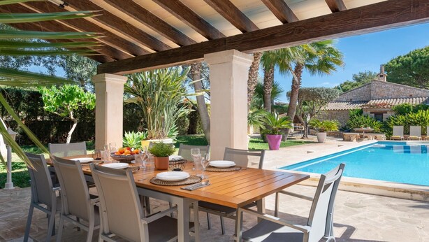 A covered outdoor dining area with a pool in the background.