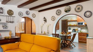 A cozy living room with a yellow sofa, a dining area with a table and chairs, and a kitchen visible through an archway.