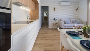 Una cocina moderna con armarios blancos y encimera de madera, que da a un comedor con una mesa blanca preparada para dos.