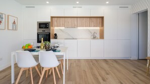 Una cocina moderna con armarios blancos, detalles de madera y un comedor con mesa y sillas blancas.