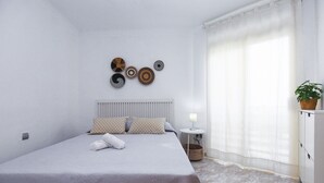 A neatly arranged bedroom with a bed, pillows, a bedside table with a lamp, and wall art. - FUENTE Beachfront Apartment (Salou)