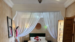 A bedroom with a bed, two sofas, a wooden table, and a decorative mirror. - Riad Les Miroires (Marrakech)