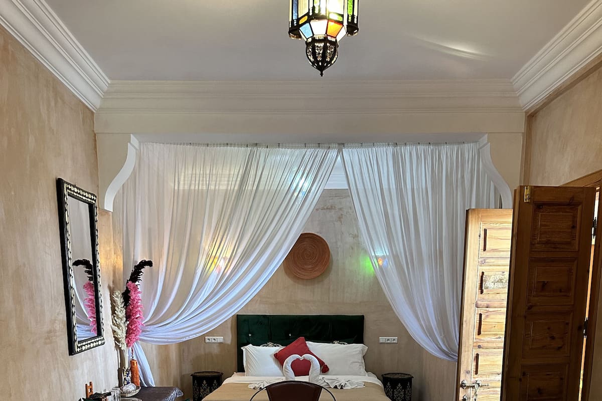 A bedroom with a bed, two sofas, a wooden table, and a decorative mirror.