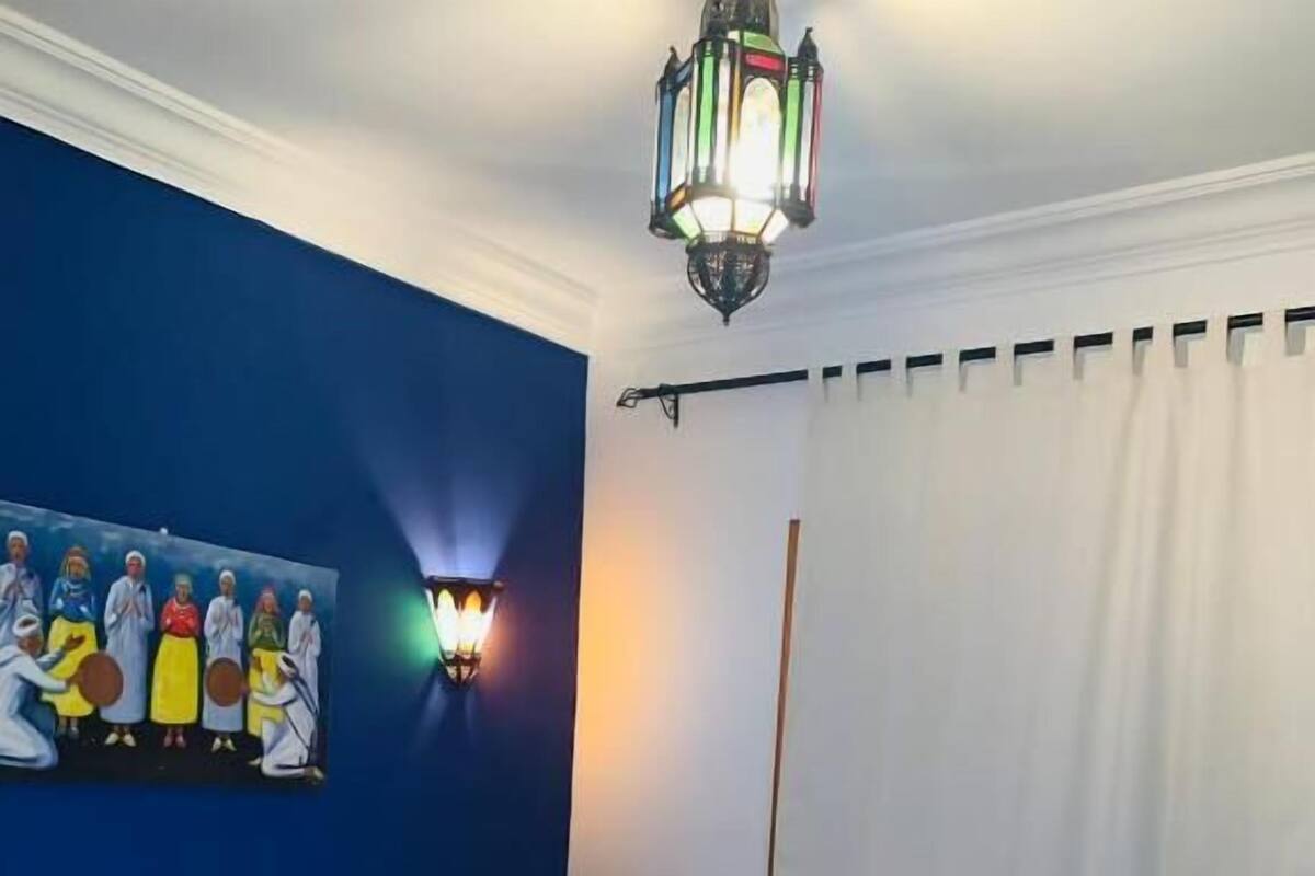 A hotel room with a bed, a painting on the wall, a wall-mounted light fixture, and a window with curtains.