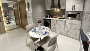 A modern kitchen with a built-in oven, microwave, and dishwasher. There is a dining area with a table set for two, and a washing machine in the corner. - Mehad Stay for Self Check-In Apartment (Jeddah)
