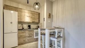 Eine moderne Küche mit Holzschränken, einem weißen Kühlschrank, einer Kaffeemaschine und einem Essbereich mit Tisch und Stühlen.
