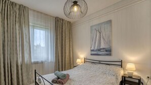 Ein Schlafzimmer mit Bett, Vorhängen, einem Gemälde, einer Lampe und einem Nachttisch.