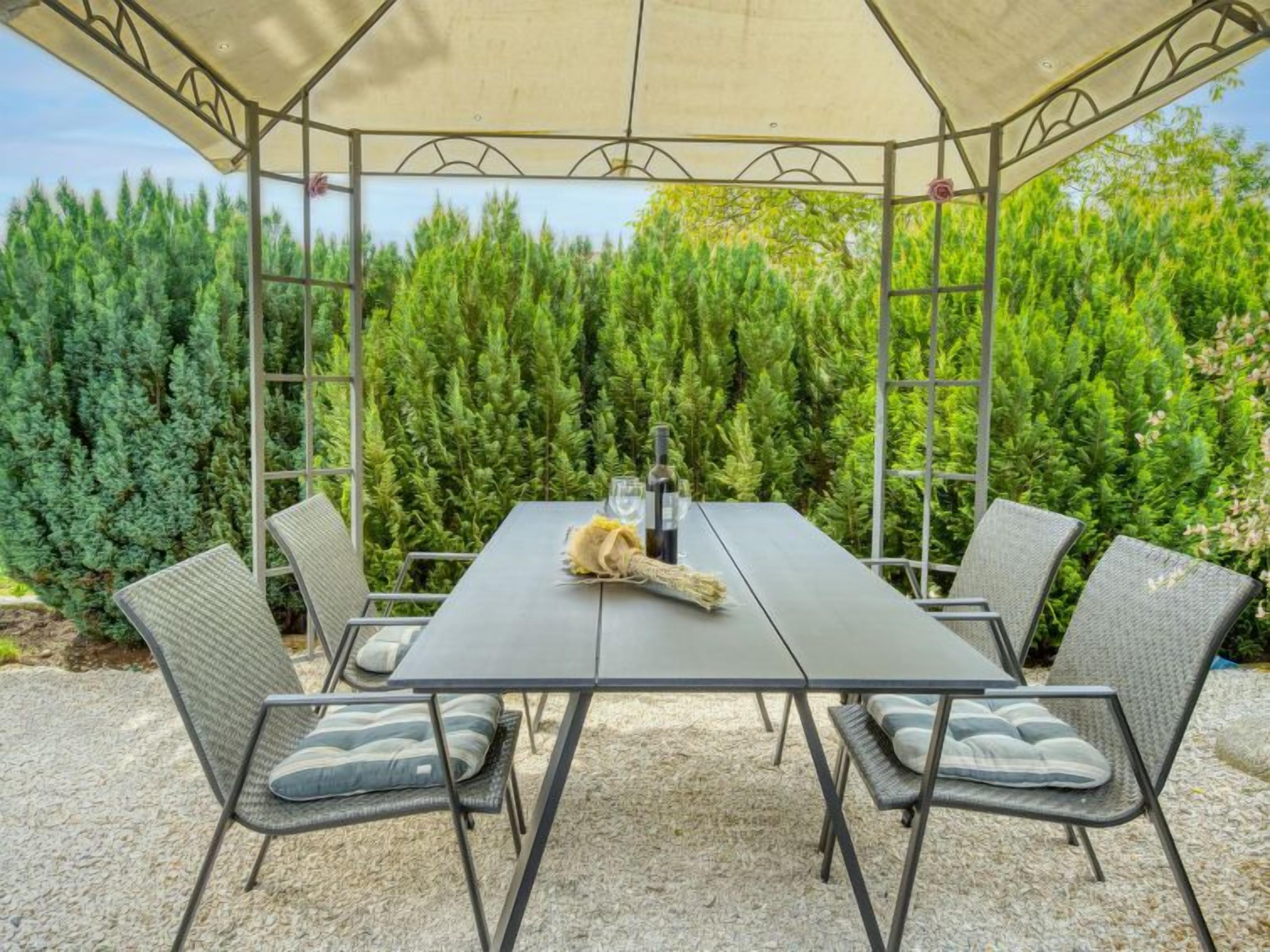 Un espace extérieur aménagé, abrité et doté d’une table et de chaises, entouré d’une végétation luxuriante.