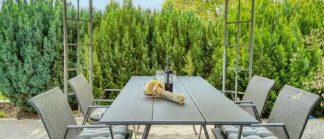 Un espace extérieur aménagé, abrité et doté d’une table et de chaises, entouré d’une végétation luxuriante.