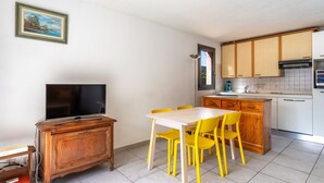 Een compacte woonruimte met een eethoek, kitchenette en een televisie op een houten kast.