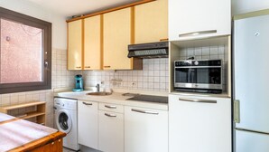 Een praktische keuken met witte kastjes, een inbouwoven, een wasmachine en een raam met uitzicht op het omliggende landschap.