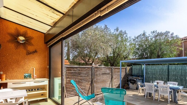 Een terras met een tafel, stoelen, een barbecue en een blauwe opklapbare stoel.
