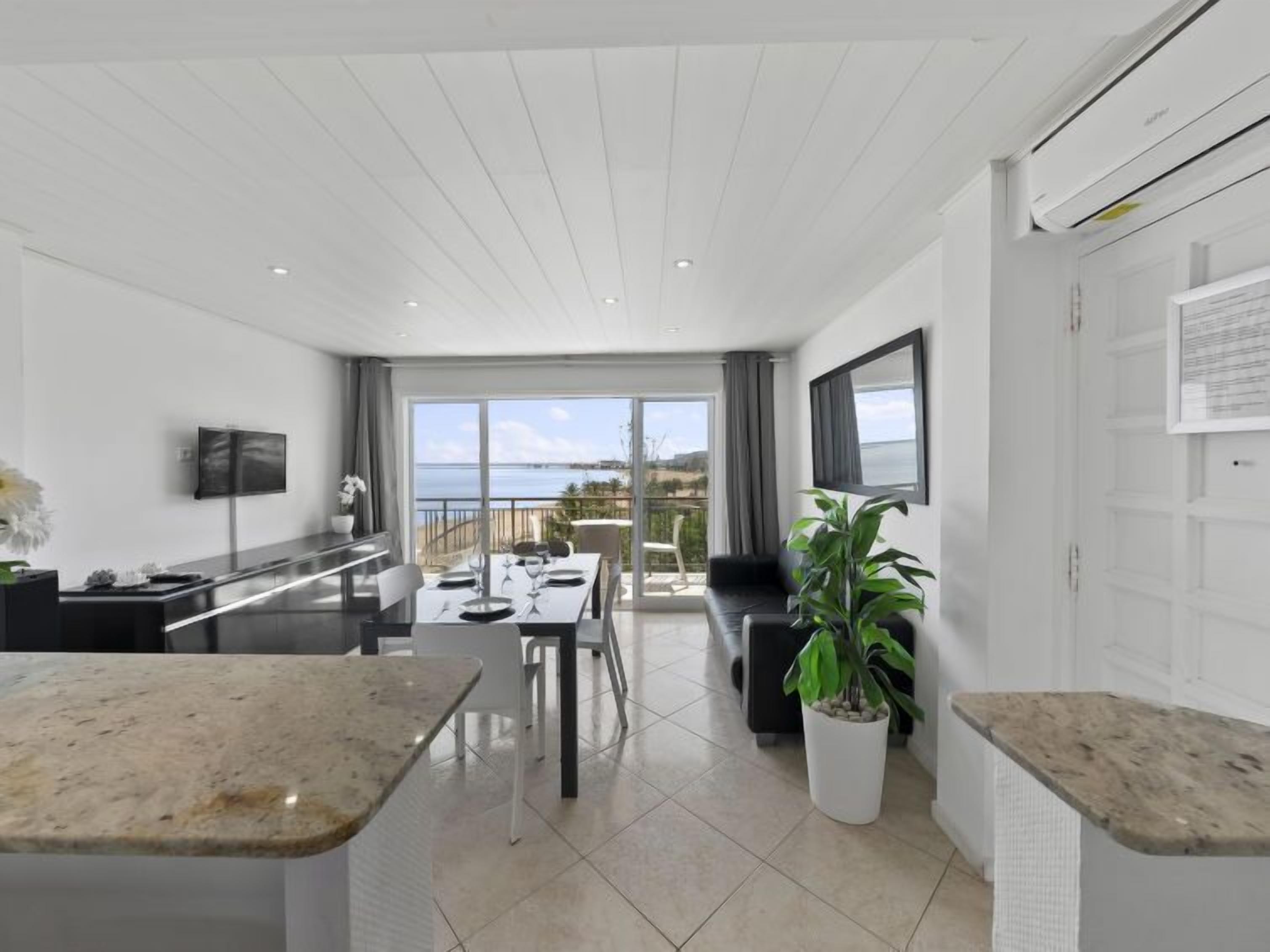 A modern kitchen with a dining area, large windows, and a view of the sea.