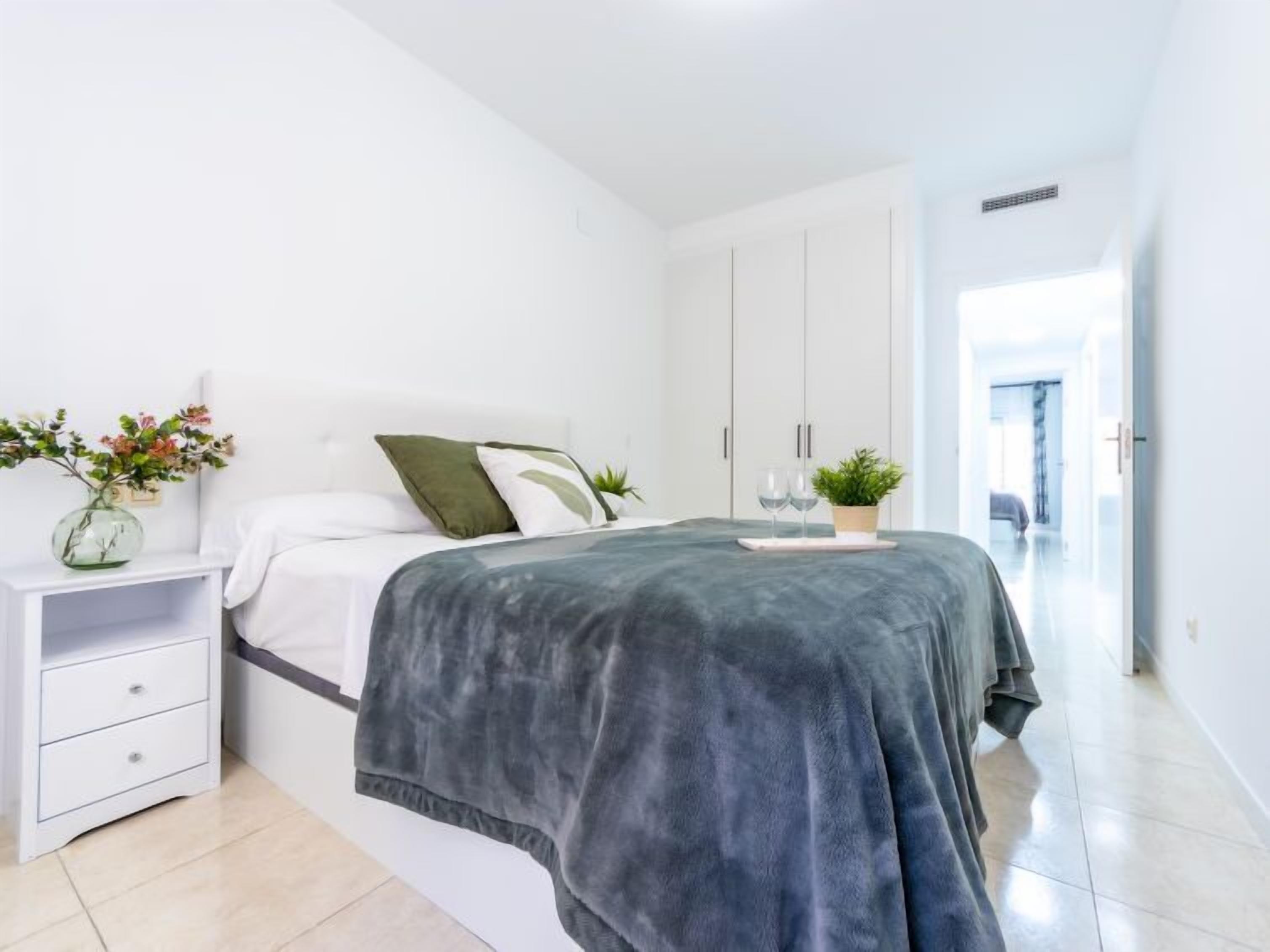 Une chambre à coucher avec un lit, une table de chevet, une plante en pot et un vase rempli de fleurs.