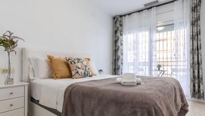 Un dormitorio moderno con cama, mesita de noche, cómoda y ventana con cortinas.