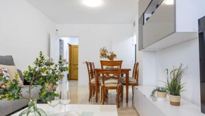 Una sala moderna con comedor, que presenta una mesa de madera, sillas, un sofá y un televisor montado en la pared.