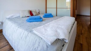Un lit bien fait, recouvert d’une couvre-lit blanche et bleue à motifs, avec deux serviettes bleues enroulées et un coussin décoratif blanc.