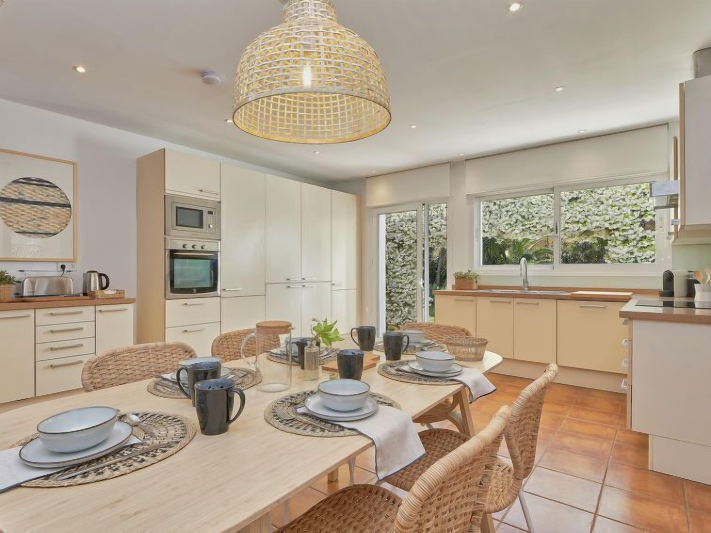 A modern kitchen with white cabinets, a dining table set with plates, cups, and a chandelier.