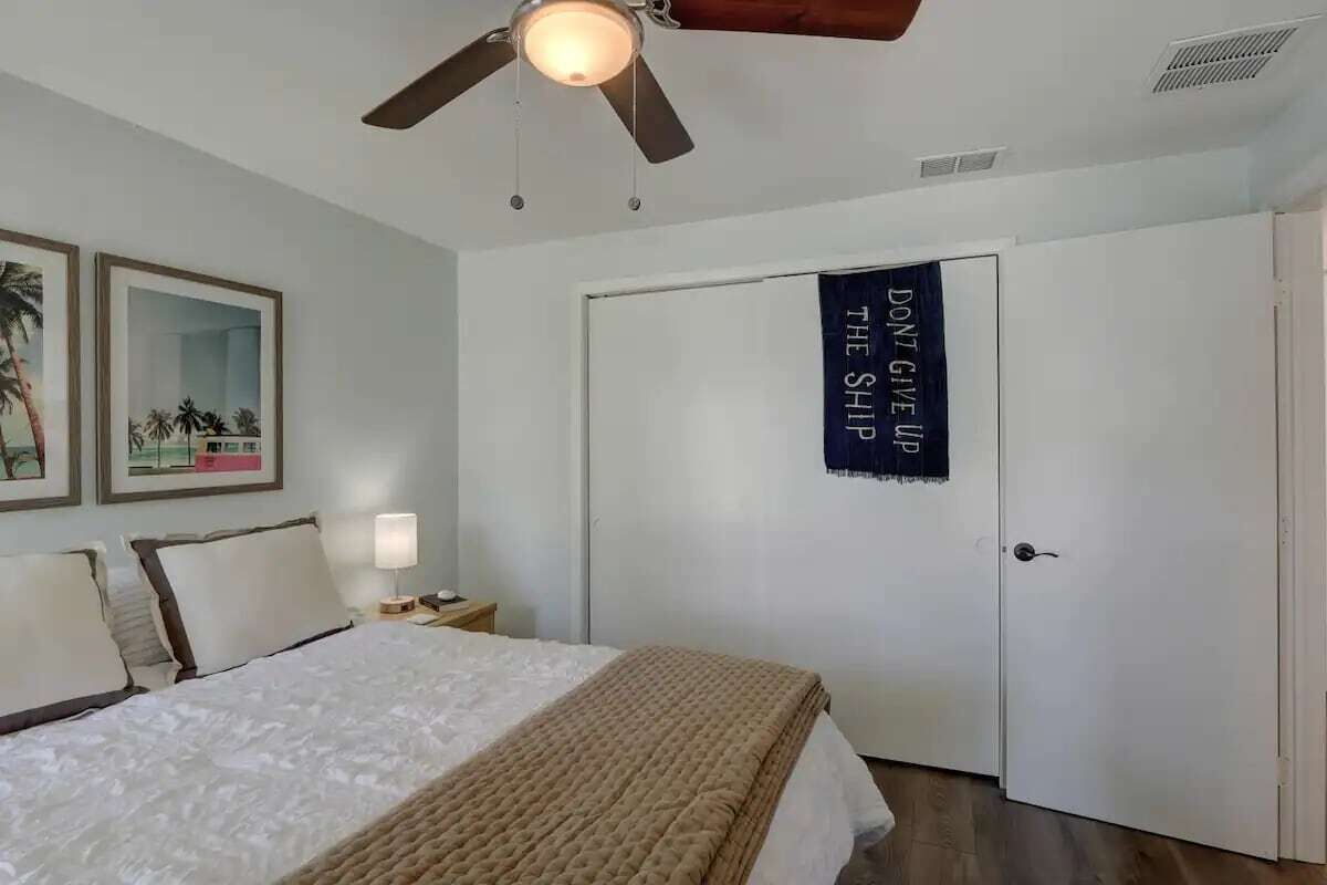 A bedroom with a bed, a nightstand, a ceiling fan, and a door with a motivational poster.
