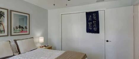 A bedroom with a bed, a nightstand, a ceiling fan, and a door with a motivational poster.