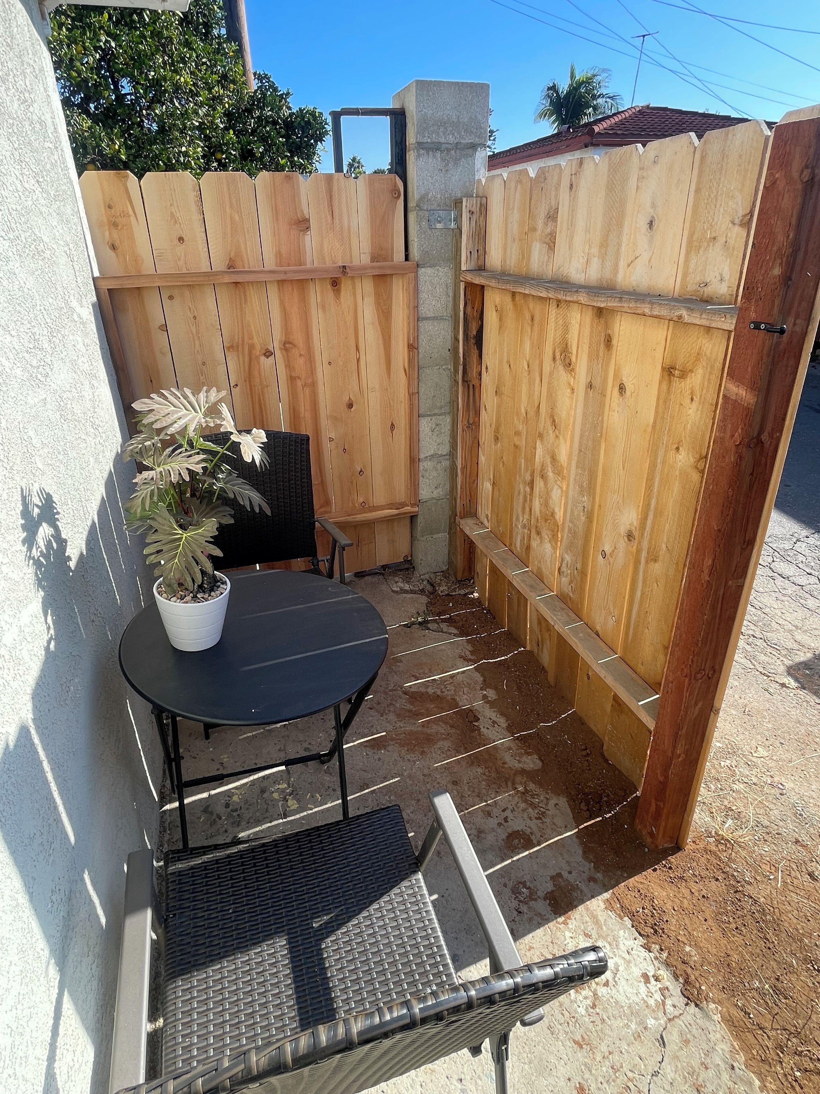 A small outdoor patio with a table and chairs, a potted plant, and a wooden fence.